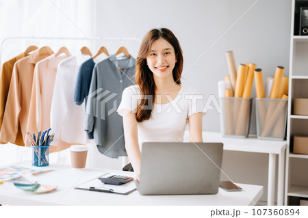 Asian tailor woman working on clothes in tailoring atelier. beautiful young female fashion designer smile and after success in modern studio Asian tailor woman working on clothes in tailoring atelier. beautiful young female fashion designer smile and after success in modern studio 107360894