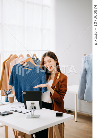 Fashion blogger concept, Young Asian women selling clothes on video streaming.Startup small business SME, using smartphone or tablet taking receive and checking. Fashion blogger concept, Young Asian women selling clothes on video streaming.Startup small business SME, using smartphone or tablet taking receive and checking. 107360974