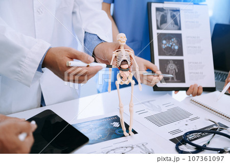 Medical team having a meeting with doctors in white lab coats and surgical scrubs seated at a desk discussing a patients working online using computers in the medical industry. 107361097