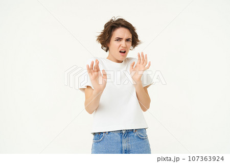 Young woman raises hands up and refuses, rejects smth, tried to block something disgusting, standing over white background Young woman raises hands up and refuses, rejects smth, tried to block something disgusting, standing over white background 107363924