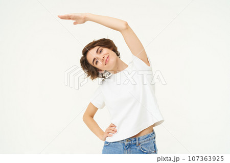 Portrait of woman doing exercise, fitness movements, bending arm sideways and stretching body, standing over white background Portrait of woman doing exercise, fitness movements, bending arm sideways and stretching body, standing over white background 107363925