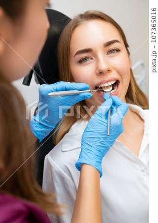 Female Patient in Dental Chair for Treatment, Dentist Examining Front Teeth for Strength 107365016