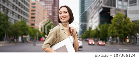 Outdoor shot of asian girl with laptop, going somewhere in city centre, walking on street, going to work 107366124