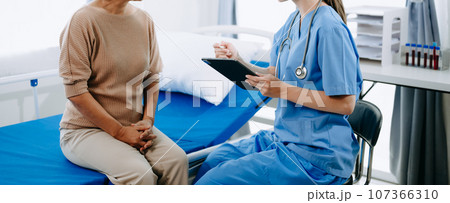 Doctor and senior female patient who lie on the bed while checking pulse, consult and explain with nurse taking note in hospital wards or clinic.. Doctor and senior female patient who lie on the bed while checking pulse, consult and explain with nurse taking note in hospital wards or clinic.. 107366310
