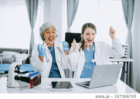 Medical team having a meeting with doctors in white lab coats and surgical scrubs seated at a table discussing a patients working online using computers in the medical industry.. Medical team having a meeting with doctors in white lab coats and surgical scrubs seated at a table discussing a patients working online using computers in the medical industry.. 107366745