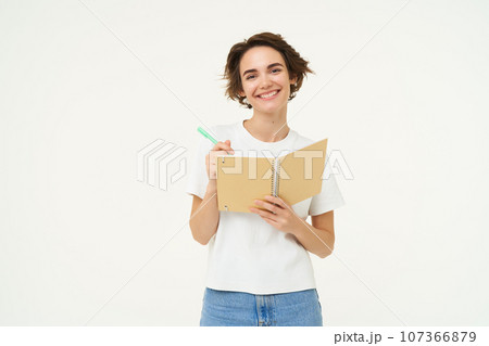 Portrait of smiling, beautiful and creative woman, holding pen and notebook, writing in her planner, has a diary, posing over white studio background Portrait of smiling, beautiful and creative woman, holding pen and notebook, writing in her planner, has a diary, posing over white studio background 107366879
