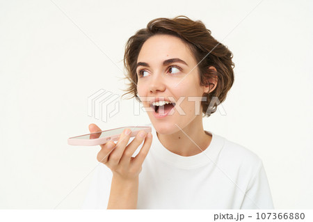 Portrait of woman talking into mobile phone speakerphone, records voice message, translates words, stands over white background Portrait of woman talking into mobile phone speakerphone, records voice message, translates words, stands over white background 107366880
