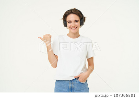 Portrait of brunette woman, smiling with confidence, pointing finger left, showing advertisement, standing over white background Portrait of brunette woman, smiling with confidence, pointing finger left, showing advertisement, standing over white background 107366881
