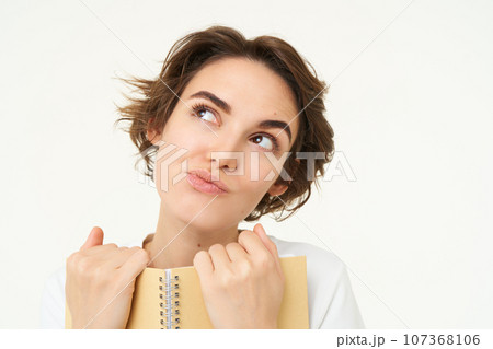 Portrait of happy, beautiful woman holding planner, making notes, doing her homework, standing over white background Portrait of happy, beautiful woman holding planner, making notes, doing her homework, standing over white background 107368106