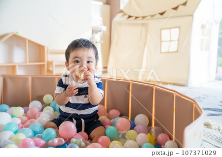 自然光の室内でボールプールに入れられて楽しそうに遊ぶ0歳生後10か月の赤ちゃん 107371029