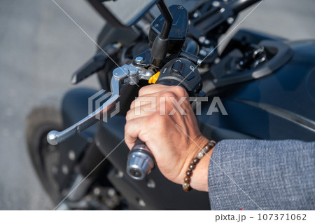 Caucasian man rides an electric motorcycle. Close-up of a man's hand pressing the gas on the steering wheel.  107371062