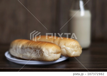 Bread on a white plate sits on a wooden board table with milk in a bottle behind it 107372982