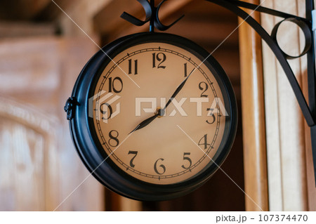 Round vintage clock in black metal hanging on corner mount on wooden wall. Decorative elements. Round vintage clock in black metal hanging on corner mount on wooden wall. Decorative elements. 107374470