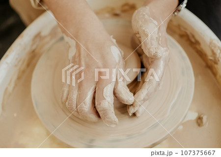 woman sculpts from clay. modeling on a potter's wheel. Hands are molded from clay. Creative workshop. The girl sculpts from clay. Working atmosphere in the workshop. woman sculpts from clay. modeling on a potter's wheel. Hands are molded from clay. Creative workshop. The girl sculpts from clay. Working atmosphere in the workshop. 107375667
