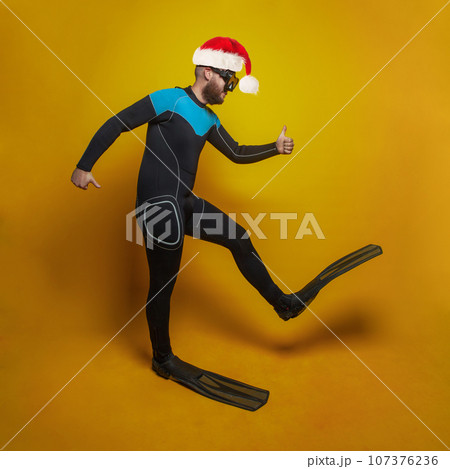 Christmas or New Year holidays concept. Diver in red Santa hat on yellow studio wall background Christmas or New Year holidays concept. Diver in red Santa hat on yellow studio wall background 107376236