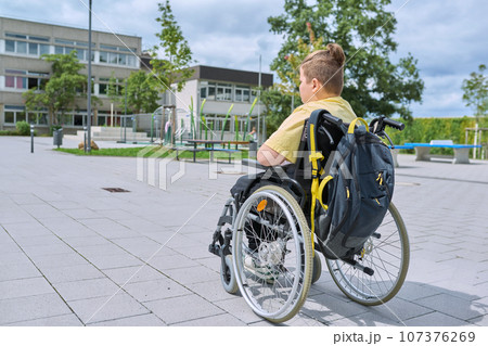 Back view, child preteen boy on wheelchair going to school building 107376269