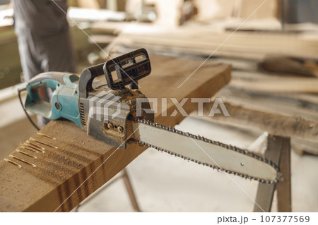 Professional electric chainsaw lies on a wooden plank in the carpentry workshop Professional electric chainsaw lies on a wooden plank in the carpentry workshop 107377569