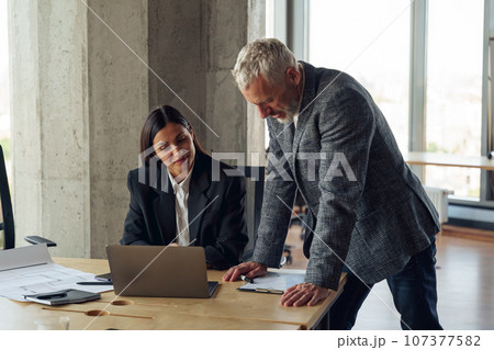 Senior male boss discussing online project with employee showing presentation to team leader Senior male boss discussing online project with employee showing presentation to team leader 107377582