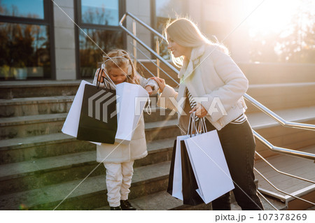Young mother and little girl with shopping bags after shopping. Spring Style. Consumerism. 107378269