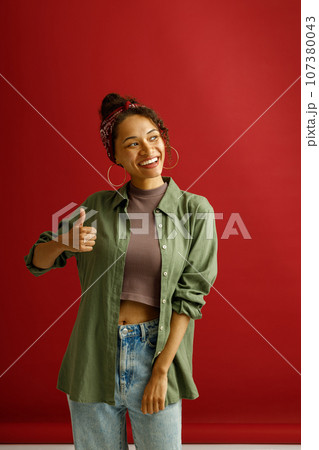 Positive woman showin thumbs up with smile while standing over red studio background 107380043