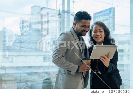 Two happy diverse coworker discussing report on tablet, working on project together Two happy diverse coworker discussing report on tablet, working on project together 107380536