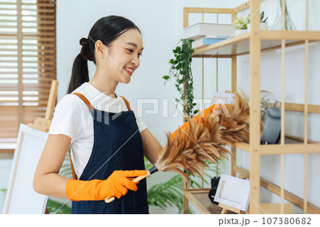 Asian young housework cleaning working in the house. The woman cleans the shelf wood with feather duster Asian young housework cleaning working in the house. The woman cleans the shelf wood with feather duster 107380682