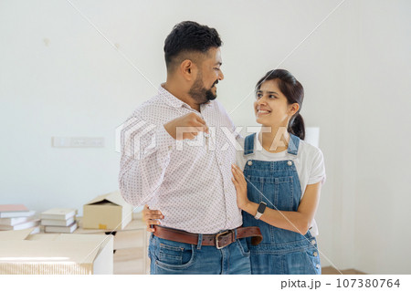 House Ownership. Portrait Of Happy Indian Married Holding Showing Key Standing In New home House Ownership. Portrait Of Happy Indian Married Holding Showing Key Standing In New home 107380764