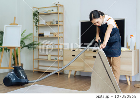 young woman housework lifting the carpet to vacuum with a vacuum cleaner young woman housework lifting the carpet to vacuum with a vacuum cleaner 107380858