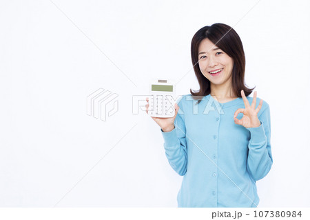 白い背景の前で電卓を持ちOKサインをしている30代の女性 107380984