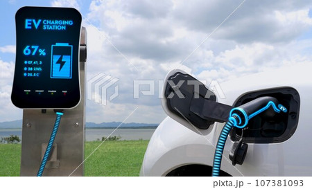 Electric car plugged in with charging station with nature background. Peruse Electric car plugged in with charging station with nature background. Peruse 107381093