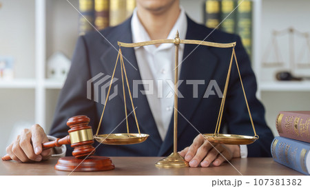 Lawyer man hold a judge's gavel and law scale and books beside in law office 107381382