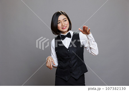 Catering service cheerful smiling asian woman employee dancing. Carefree joyful young waitress wearing uniform making moves with hands while posing in studio on gray background 107382130