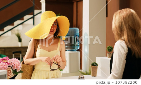 Woman guest arriving at hotel front desk, talking about room reservation at tropical seaside resort. Summertime traveller checking in at exotic islands hotel, international vacation. 107382200