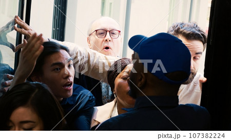 Mad shoppers breaking into shop during black friday promotions at shopping center, pushing security guard and asking for store access. Anxious aggressive people outside front door. Handheld shot. 107382224