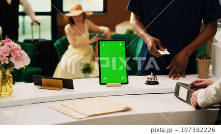Hotel concierge service with greenscreen, modern tropical resort front desk with isolated mockup template on digital tablet. Receptionist working in hotel lobby with blank copyspace. 107382226
