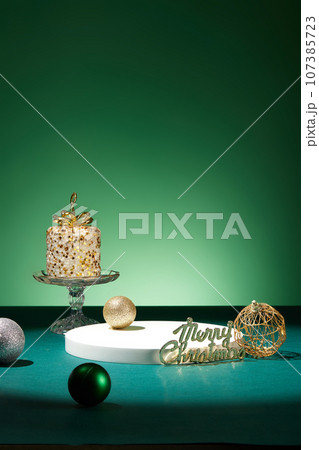 A scented candle decorated with colorful baubles and the inscription merry christmas. Modern minimal showcase scene for cosmetic products promotion 107385723