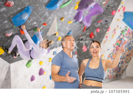 Adult man and young woman posing on climbing wall Adult man and young woman posing on climbing wall 107385991