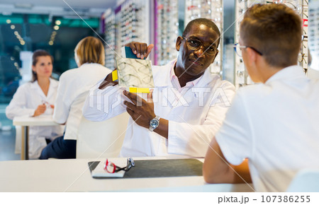 African-American ophthalmologist showing mirror to teen boy 107386255