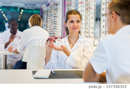 Ophthalmologist and cheerful young boy choosing glasses Ophthalmologist and cheerful young boy choosing glasses 107386303