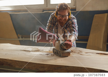 Professional male carpenter using electric sander for wood. Manufacture of wood products Professional male carpenter using electric sander for wood. Manufacture of wood products 107387083