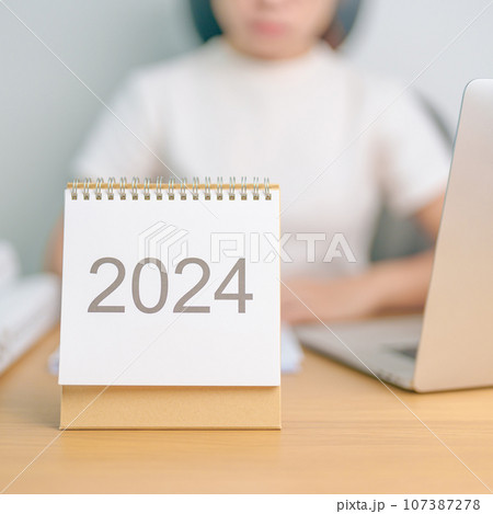 2024 Year Calendar on table with business woman using laptop computer. countdown, Happy New Year, Resolution, Goals, Plan,  Action, Mission and financial Concept 107387278