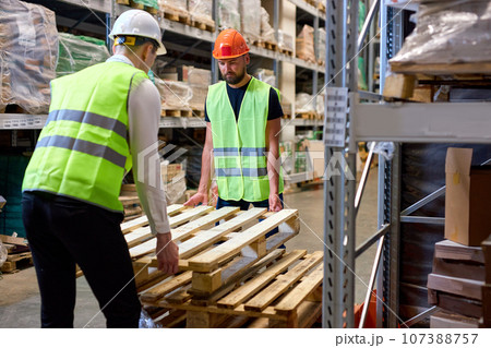 confident warehouse men hold cargo pallet together with co-worker in workplace area confident warehouse men hold cargo pallet together with co-worker in workplace area 107388757