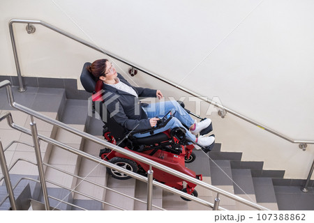 Caucasian woman in electric caterpillar wheelchair climbs up stairs. Caucasian woman in electric caterpillar wheelchair climbs up stairs. 107388862