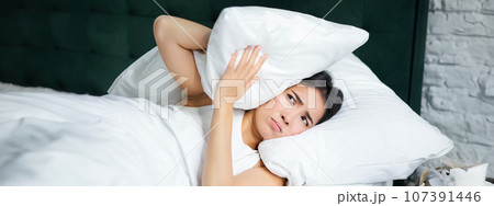 Insomnia. Asian girl shuts her ears with pillow as partner snoring. Woman lying in bed, bothered by noise at night, cannot sleep Insomnia. Asian girl shuts her ears with pillow as partner snoring. Woman lying in bed, bothered by noise at night, cannot sleep 107391446