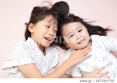 ベッドで寝転んで遊ぶ仲良しの姉妹 ベッドで寝転んで遊ぶ仲良しの姉妹 107393730