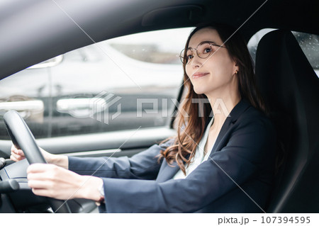 ジャケット姿で運転をするメガネをかけた若い女性 107394595
