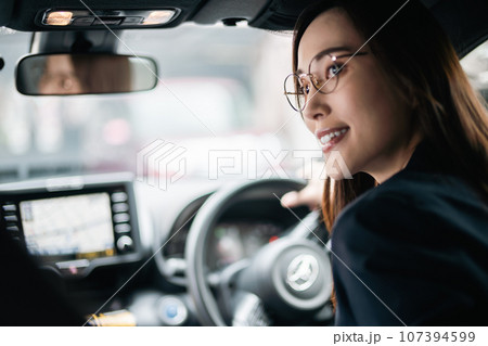 ジャケット姿で運転をするメガネをかけた若い女性 ジャケット姿で運転をするメガネをかけた若い女性 107394599