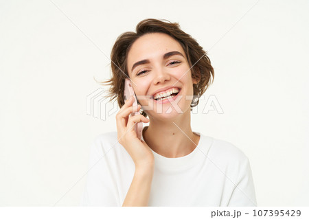 Portrait of happy, chatty young woman talking on mobile phone, using smartphone, calling someone, standing over white studio background 107395429