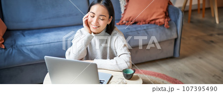 Beautiful asian girl works from home, studying with laptop, sitting in living room, being on remote, freelancing online 107395490