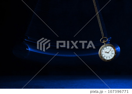 Hypnosis session. Vintage pocket watch with chain swinging over surface on dark background among faded clock faces, magic motion effect 107396771